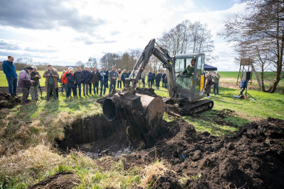 A group of people stand around an excavator at the symbolic ground-breaking ceremony